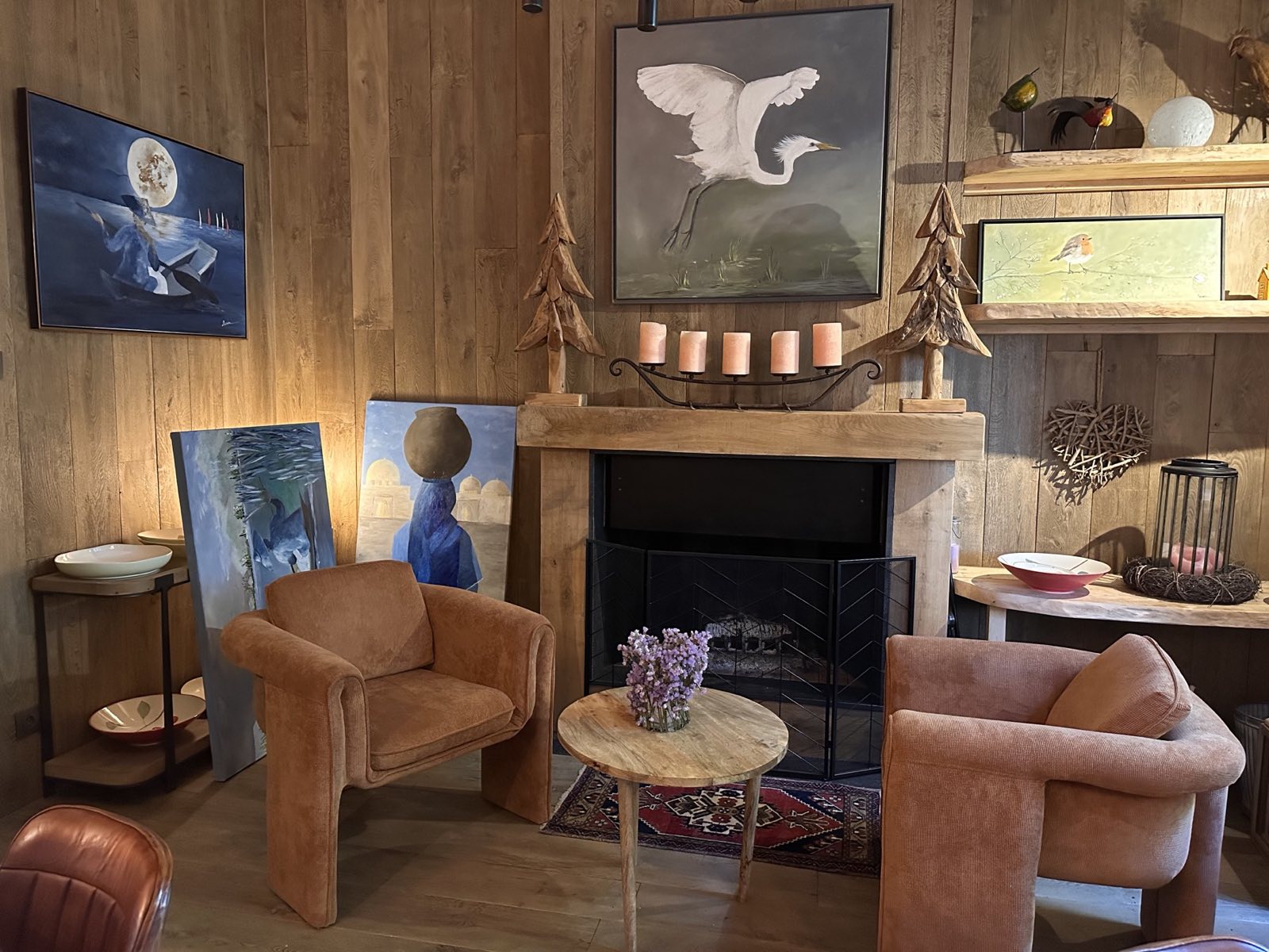 Le petit salon de La Roseraie : la cheminée, les fauteuils, et les toiles de Carine — une aigrette blanche en vol, un rouge-gorge, une femme au pot bleu